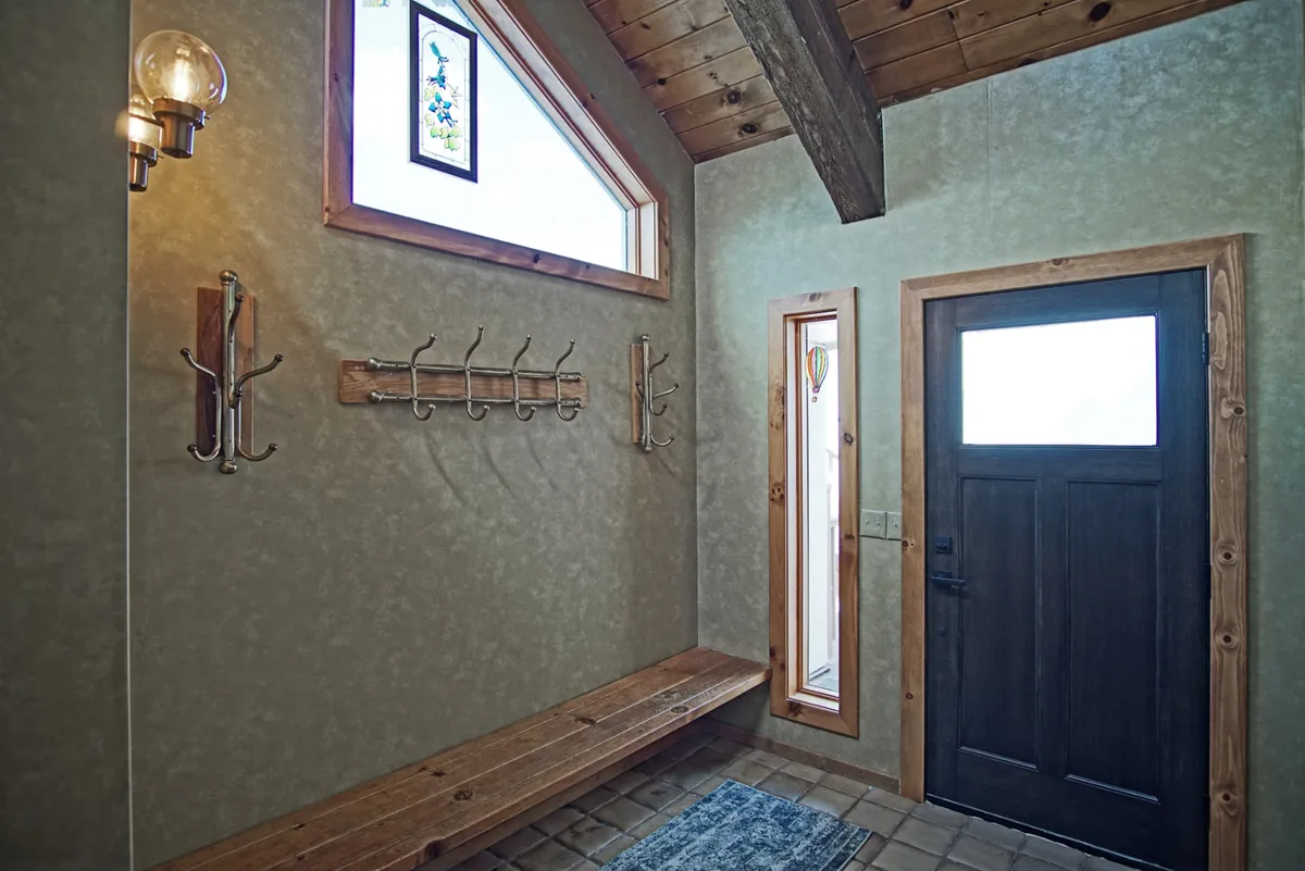 This image captures a cozy entryway featuring a wooden bench, a charming stained glass window, and the front door. The space is set up for welcoming guests, removing shoes, and storing coats, making it a practical and inviting transition zone from the outdoors into the home.