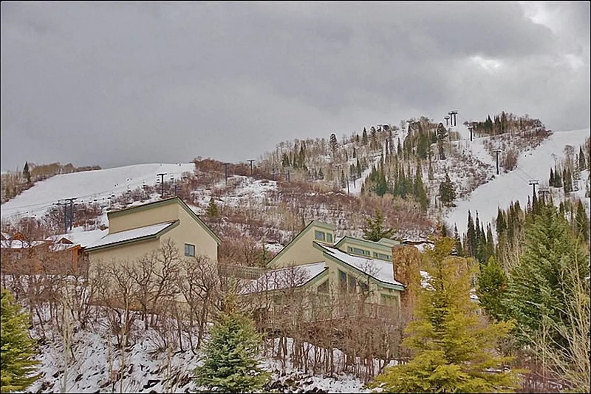 This exterior image features the ski slopes in close proximity to a building structure, surrounded by snow-dusted trees. The soft morning light illuminates the slopes, capturing the unbeatable ski-in/ski-out convenience and the chalet's immediate mountain setting.