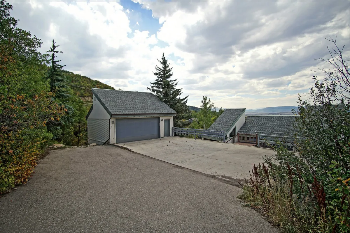 A peaceful exterior shot featuring a garage and driveway surrounded by trees, with space for guests to gather or park. The landscape suggests an accessible, welcoming home base for exploring Steamboat or hosting outdoor get-togethers.