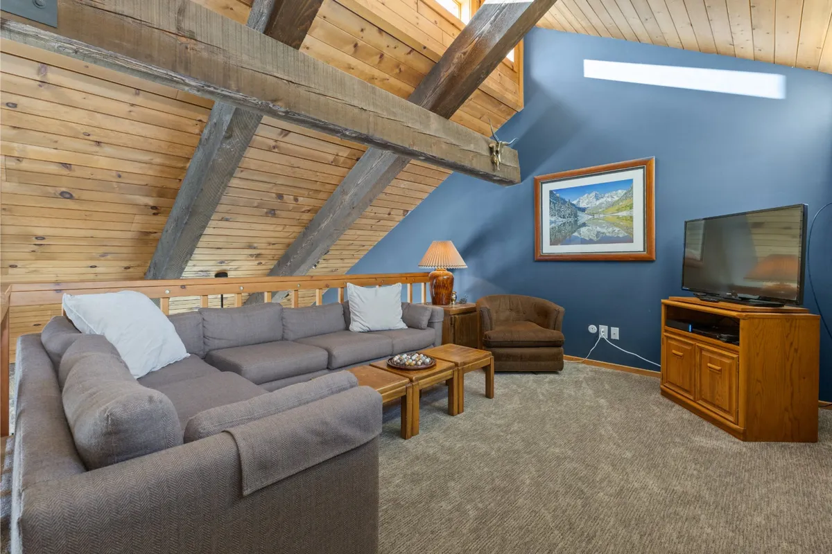 A spacious living area with a large sectional sofa, wooden coffee table, wall-mounted artwork, and a television. The room is arranged for relaxation, entertainment, and socializing, epitomizing the chalet's focus on keeping everyone connected and entertained.