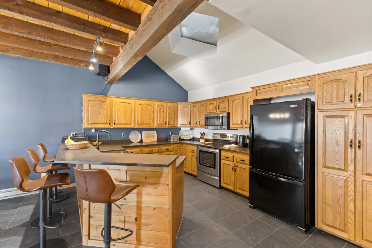 A bright, open kitchen is showcased with a large island, wooden cabinetry, modern bar stools, and a skylight above that pours natural light into the space. The inviting setup encourages group cooking, morning coffee, and lively gatherings.