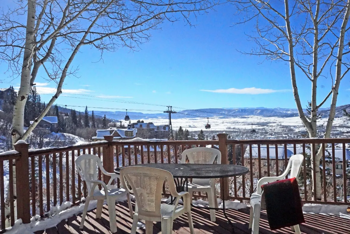 A snow-covered deck furnished with a table and chairs, offering an inviting spot overlooking distant mountain peaks. The expansive view captures the tranquility and vastness of the Yampa Valley, with the sun setting behind the mountains.
