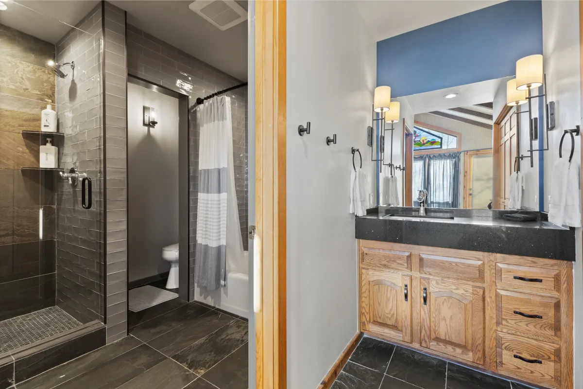 A modern bathroom featuring a walk-in shower with glass panels, a stylish vanity with a large mirror, and a decorative window. The space feels fresh and tranquil, ideal for unwinding after a day outdoors.